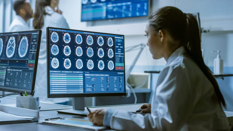 Female Medical Research Scientist Working with Brain Scans on Her Personal Computer, Writing Down Data in a Clipboard. Modern Laboratory Working on Neurophysiology, Science,  Neuropharmacology